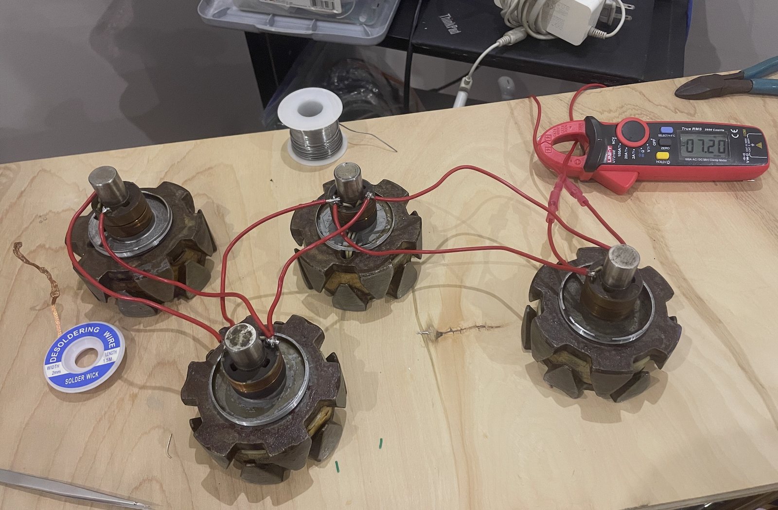 Four alternator rotors on a plywood bench, wired in parallel with red leads, a clamp meter reading 7.20 amps on the supply lead